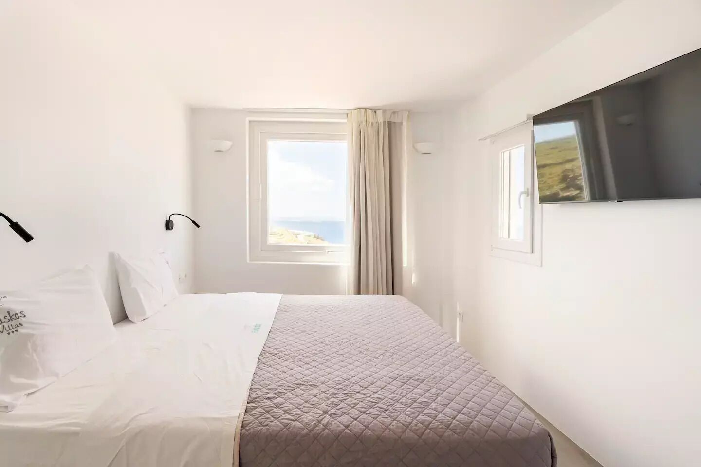 Una habitació d'hotel amb un llit, una finestra amb vista al mar i una cortina.