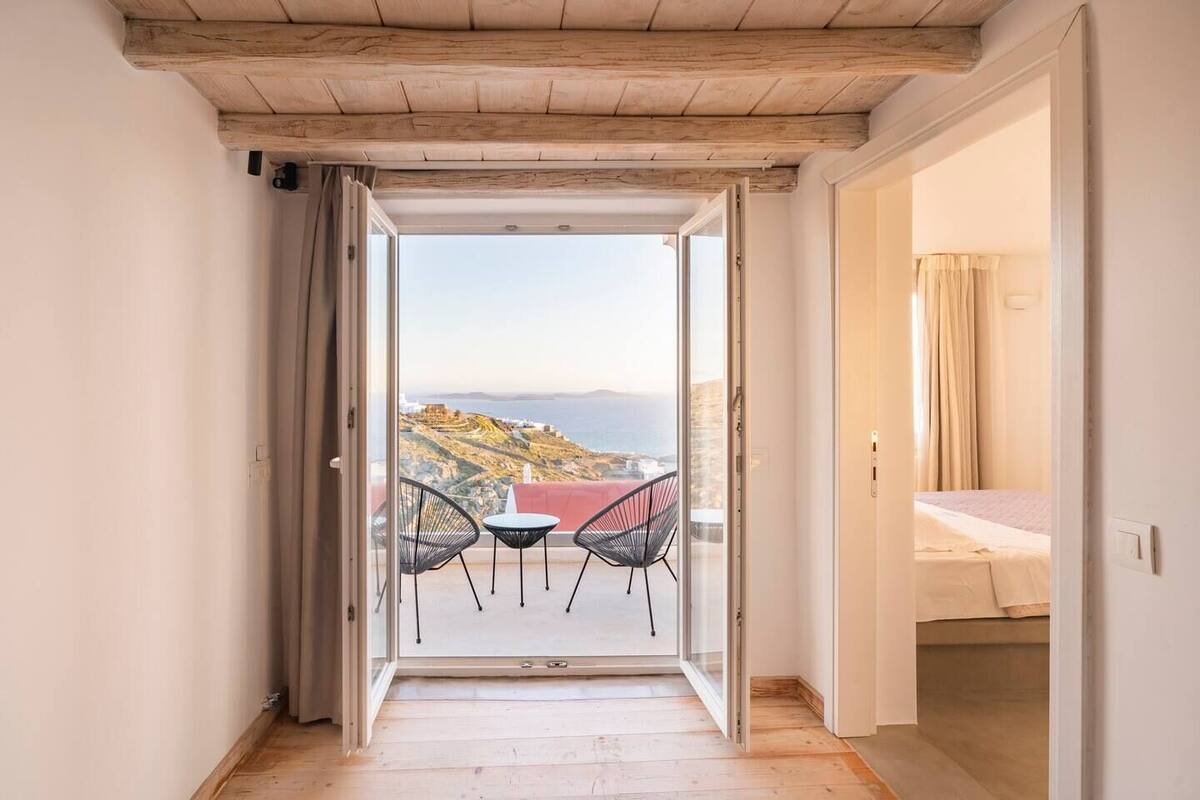 A narrow hallway leading to a balcony with a view of the sea and a bed in the adjacent room.