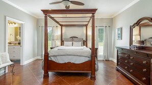 A spacious bedroom with a four-poster bed, a wooden dresser, and a ceiling fan.
