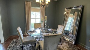 A dining area with a glass table, two upholstered chairs, a chandelier, and a large mirror on the wall.