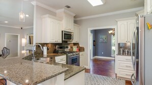 A kitchen with granite countertops, white cabinetry, stainless steel appliances, and a patterned rug.