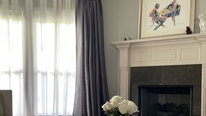 A living room with a fireplace, a sofa, a coffee table with a vase of flowers, and a painting above the mantel.