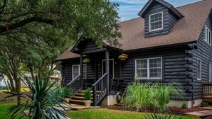 A log cabin with a porch, steps, and a small garden with plants and a wooden deck. - The Cabin - Unique OBX Stay, Huge Yard! (Kill Devil Hills)