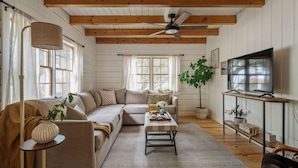 A cozy living room with a sofa, coffee table, and TV. - The Cabin - Unique OBX Stay, Huge Yard! (Kill Devil Hills)