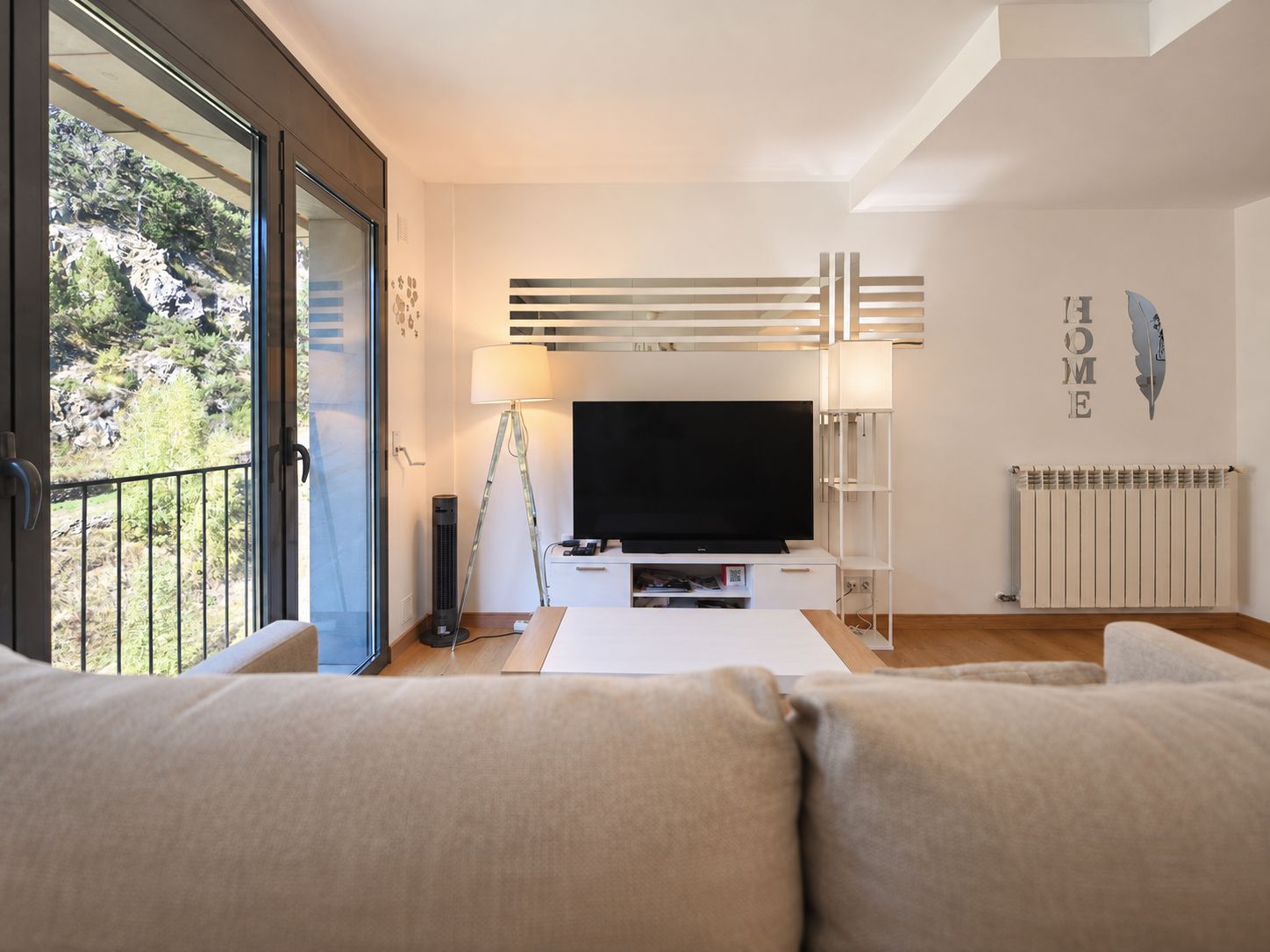 Een moderne woonkamer met een grote flatscreen televisie, een vloerlamp en een bank.