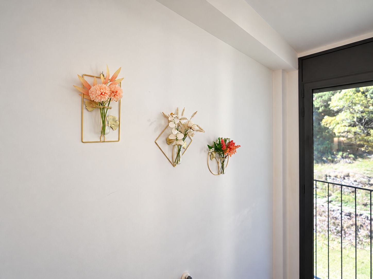 A room with three wall-mounted flower arrangements in different shapes and sizes.