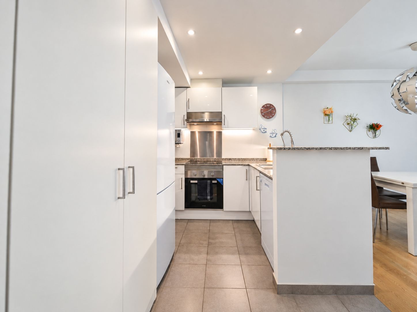 A modern kitchen with white cabinetry, stainless steel appliances, and a small dining area with a wooden table and chairs.