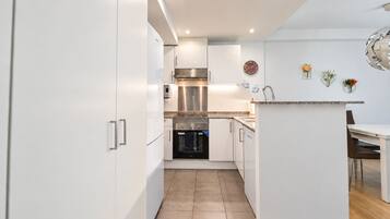 A modern kitchen with white cabinetry, stainless steel appliances, and a small dining area with a wooden table and chairs.