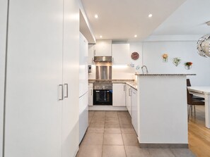 A modern kitchen with white cabinetry, stainless steel appliances, and a small dining area with a wooden table and chairs. - Riverside Shelter, Skiing, and Free Parking 
 (El Tarter)