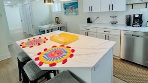 A modern kitchen with white cabinets, a stainless steel dishwasher, and a dining area with a white table and gray chairs. - Sandy Feet Retreat *A top stay in the Crest* (Wildwood Crest)