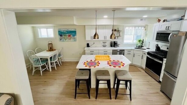 A modern kitchen with white cabinets, a central island with stools, and a dining area with white chairs. - Sandy Feet Retreat *A top stay in the Crest* (Wildwood Crest)