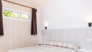 A modern bedroom with a large bed, two bedside tables, a nightstand, a window with curtains, and wall-mounted lighting. - APCOSTAS Club Torre Vella / One Bedroom (L'Estartit)
