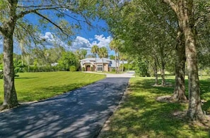 A pathway leading to a house surrounded by trees and a well-maintained lawn.