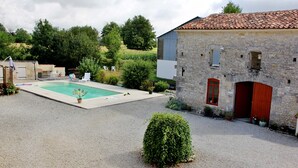 Une cour avec une piscine, des sièges d’extérieur et un bâtiment en pierre doté d’une porte rouge.