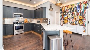 Una cucina moderna con mobili scuri, elettrodomestici in acciaio inossidabile, un'isola con piano di lavoro bianco e un murale astratto dai colori vivaci sulla parete.