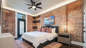 Ein Schlafzimmer mit Backsteinwand, einem Bett mit weißer Bettwäsche, einem Deckenventilator und einem Gemälde.
