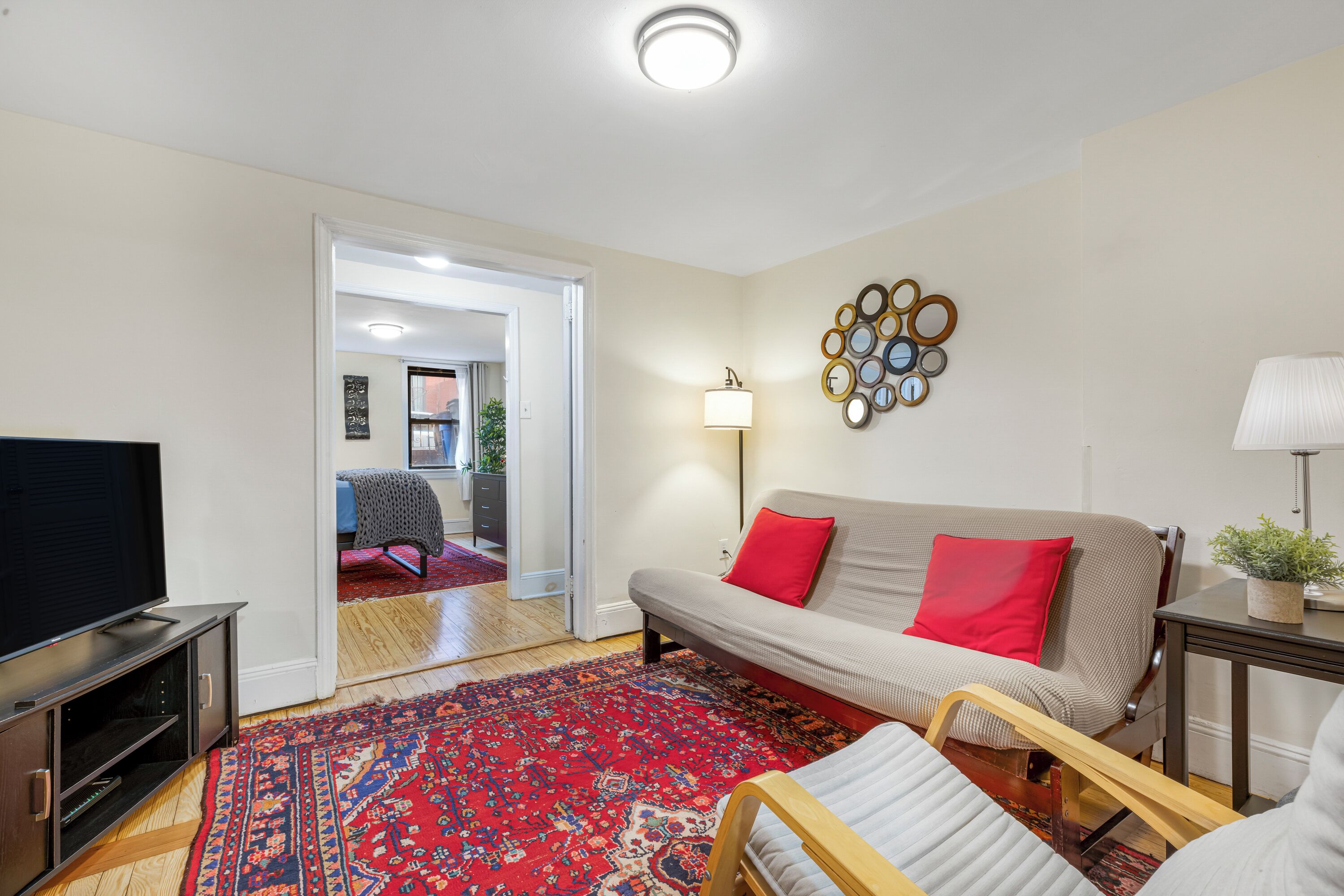 A living room with a sofa, a red rug, a television, and a wall-mounted lamp.