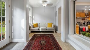 A hallway with a sofa, a red patterned rug, and a view into a kitchen area.