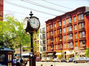 A street corner with a large clock, buildings with multiple stories, and parked cars. - Spacious Apartment Steps From NYC, Private Yard (Hoboken)