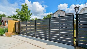 A residential area with a gated driveway, a wooden fence, and a house with a stone facade. - *EADO Urban Escape, Gated Home, Sleeps 4* (Houston)