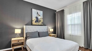 A modern bedroom with a large bed, two bedside tables, a headboard, and a window with curtains. - *EADO Urban Escape, Gated Home, Sleeps 4* (Houston)