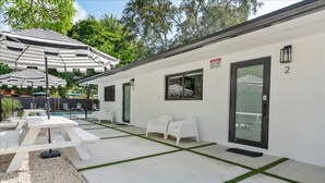 Un bâtiment blanc avec des portes numérotées, des tables à l’extérieur et des parasols.
