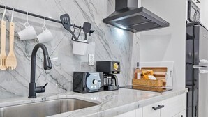 Une cuisine moderne dotée d’un plan de travail en marbre, d’un évier en acier inoxydable, d’une machine à café et d’un grille-pain.