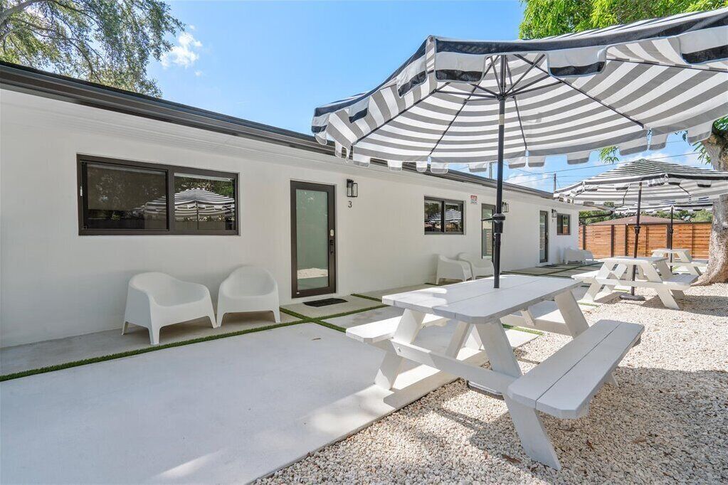 Un espace patio extérieur moderne, avec des tables et des chaises blanches, des parasols à rayures et un sol en gravier.