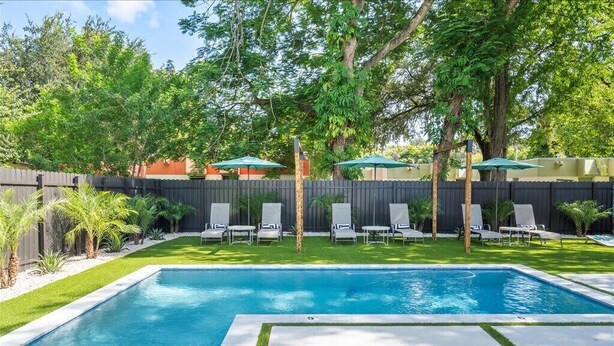 Une piscine rectangulaire avec une terrasse carrelée, entourée d’une clôture en bois et d’une végétation luxuriante.