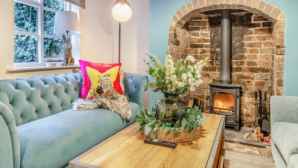 A cozy living room with a blue sofa, a fireplace, and a window with a view of trees. - The Wild Cherry Tree Retreat (Ironbridge, near Telford)