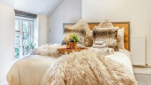 A bedroom with a large bed, fluffy pillows, a bedside table with a plant, and a window with a view of trees. - The Wild Cherry Tree Retreat (Ironbridge, near Telford)