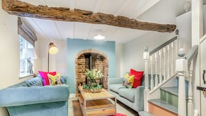 A cozy living room with a brick fireplace, two blue sofas, a wooden coffee table, and a staircase with white railings. - The Wild Cherry Tree Retreat (Ironbridge, near Telford)