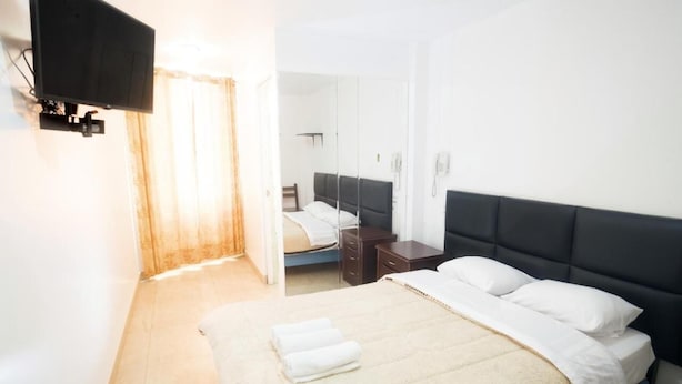 A hotel room with a bed, a flat-screen TV mounted on the wall, a bedside table, and a mirror. - hospedaje sueños (Lima)