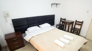 A neatly arranged bedroom with a bed, bedside table, and a small desk with chairs. - hospedaje sueños (Lima)