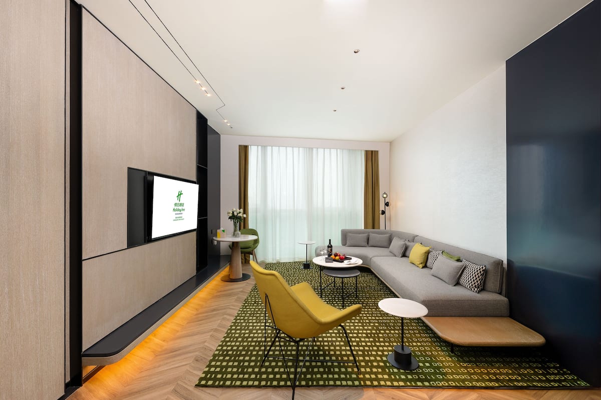 A modern living room with a sofa, a yellow armchair, a coffee table, and a flat-screen TV mounted on the wall.