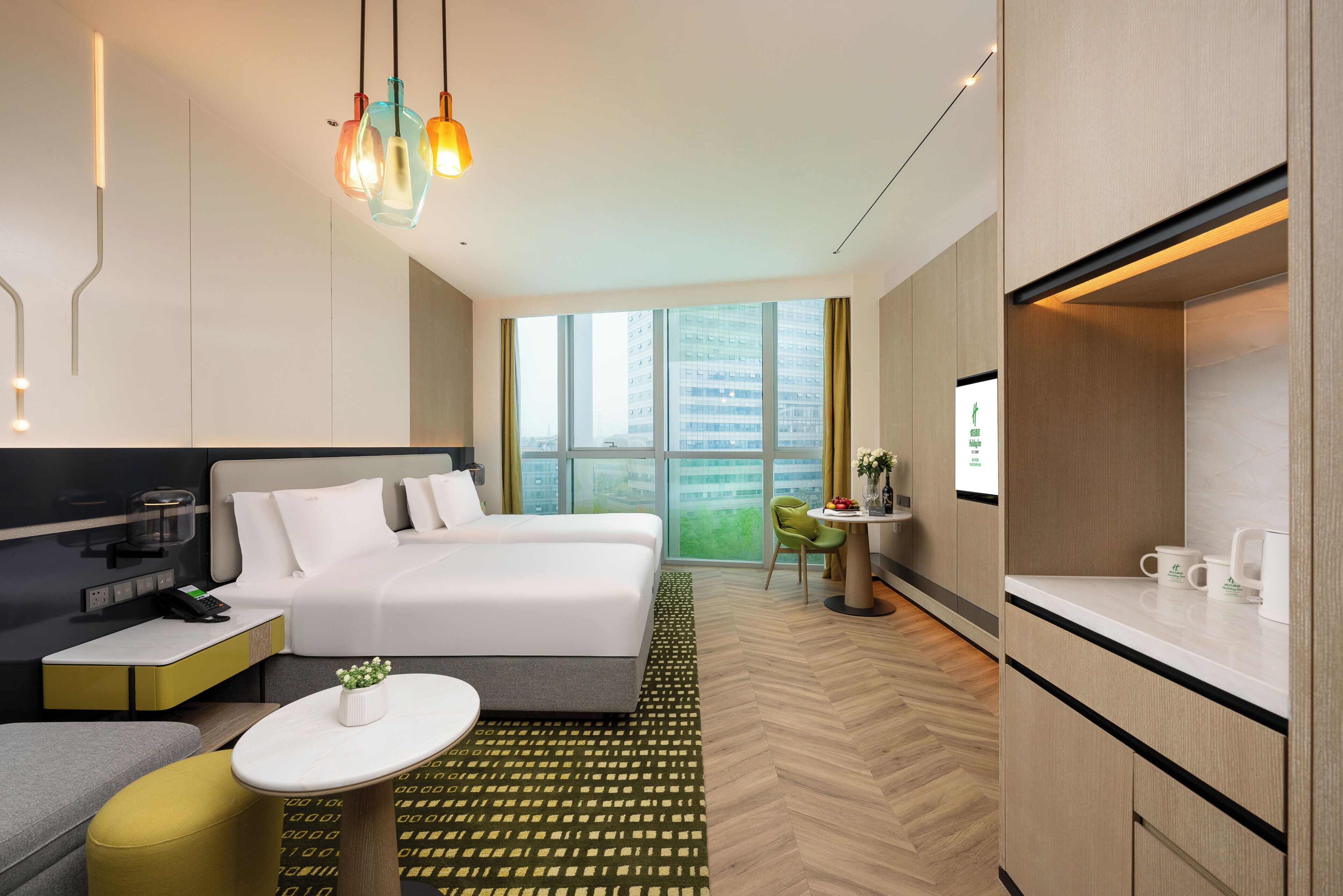A modern hotel room with a bed, bedside table, desk, and a view of the city.