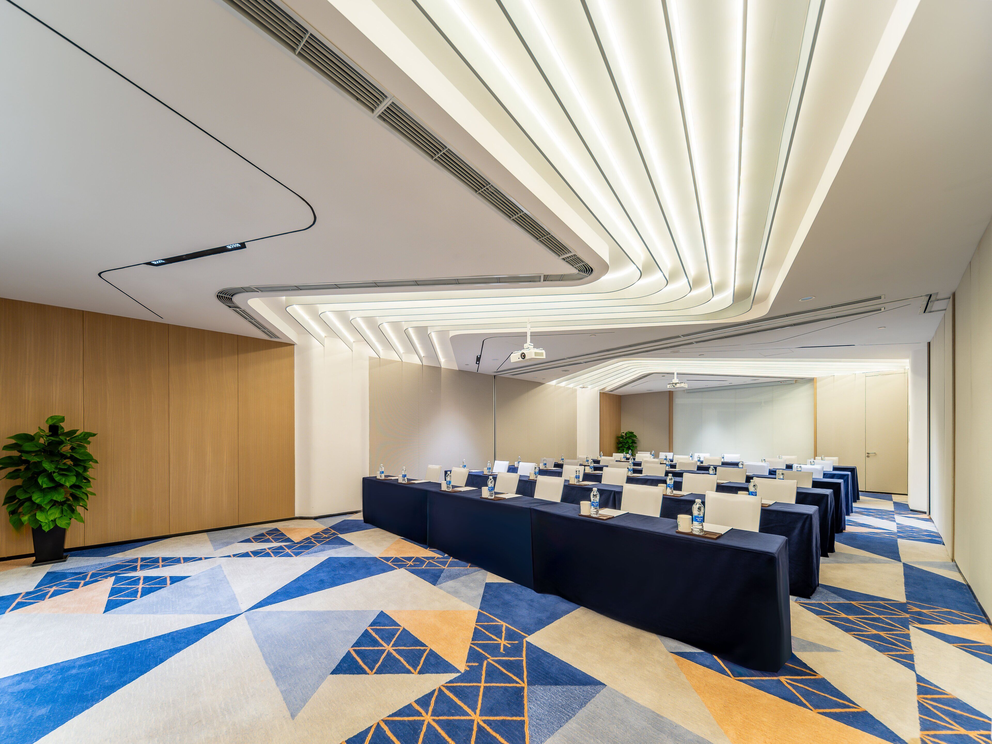 Ein Konferenzraum mit einem geometrisch gemusterten Teppich, einem langen Tisch mit Stühlen und einem modernen Deckenstil.