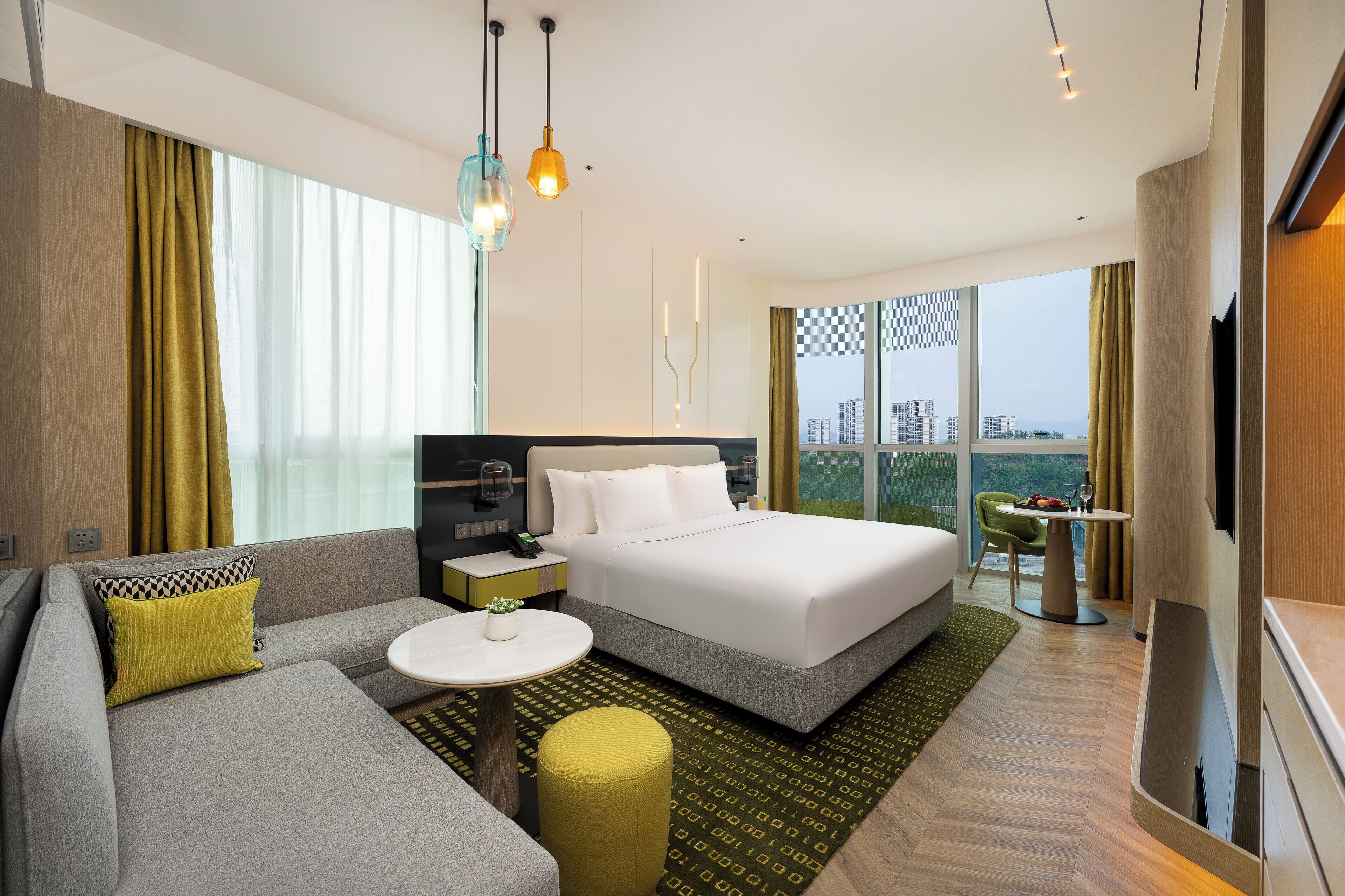 A modern hotel room with a large bed, a sofa, a small table, and a TV.