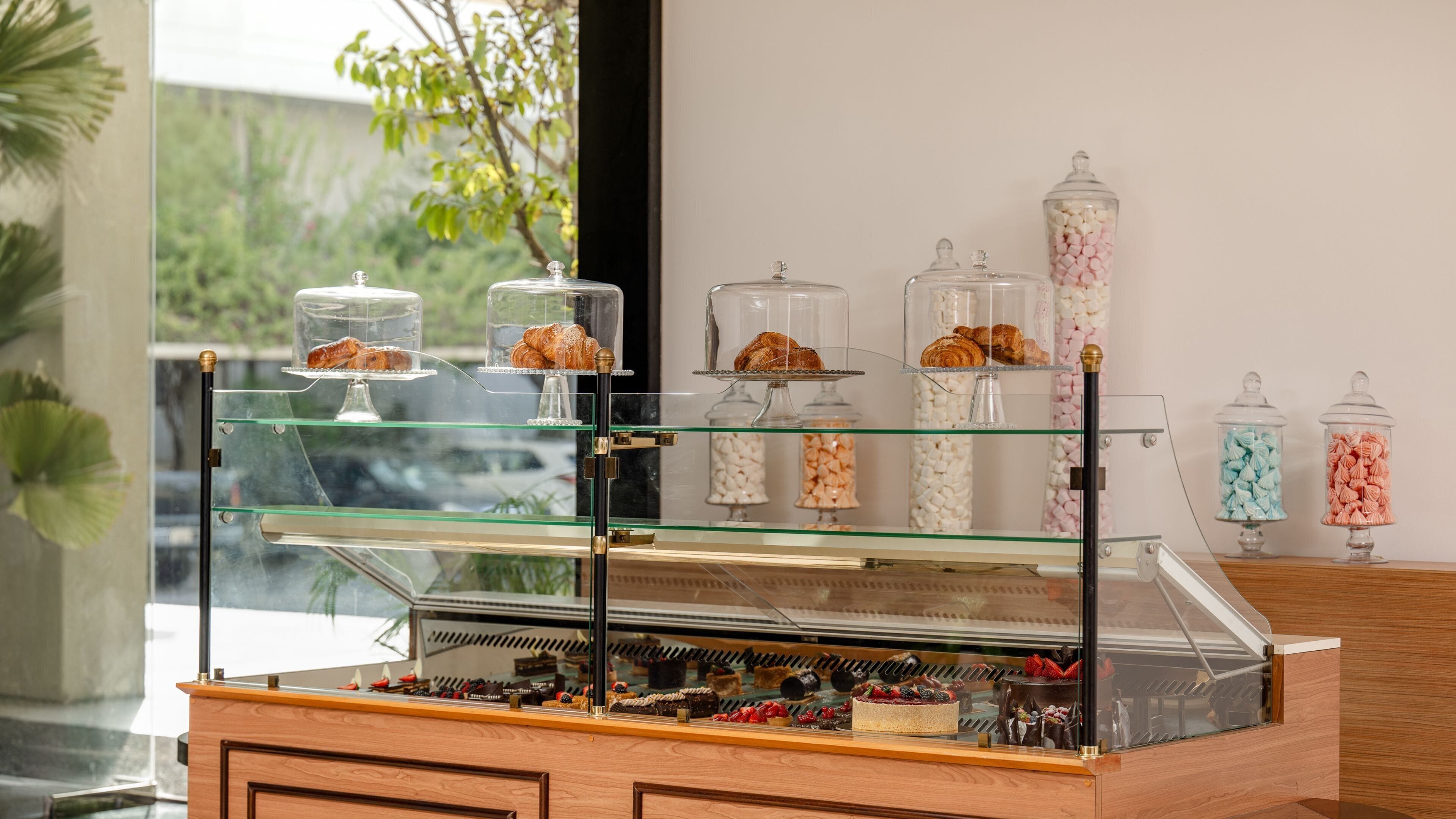 Een bakkerij vitrine met gebak en desserts, glazen potjes met snoep en een houten toonbank.