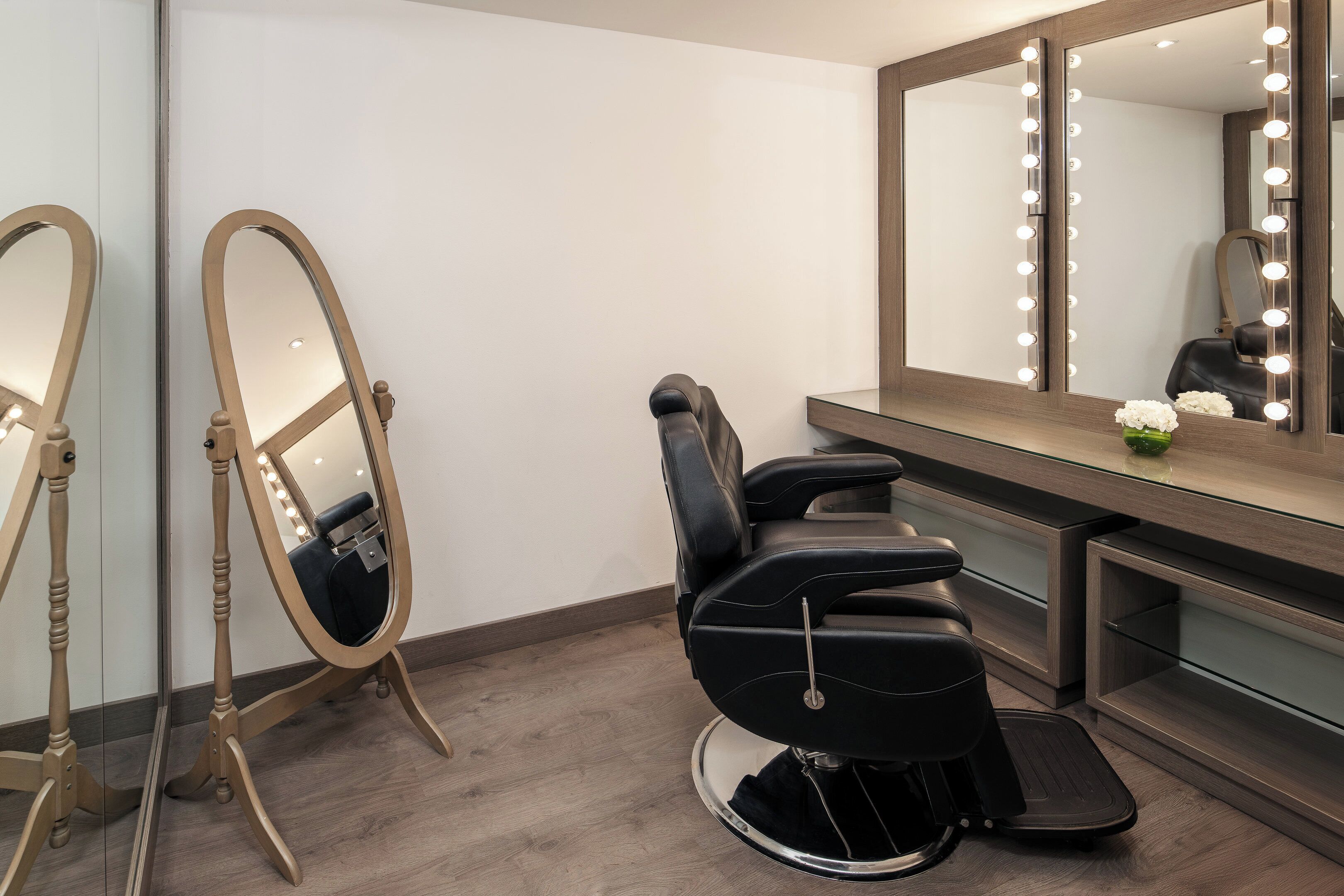 A salon with a black salon chair, a large mirror with lights, and a wooden vanity.