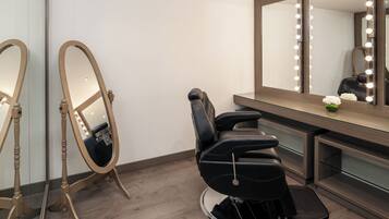 A salon with a black salon chair, a large mirror with lights, and a wooden vanity.