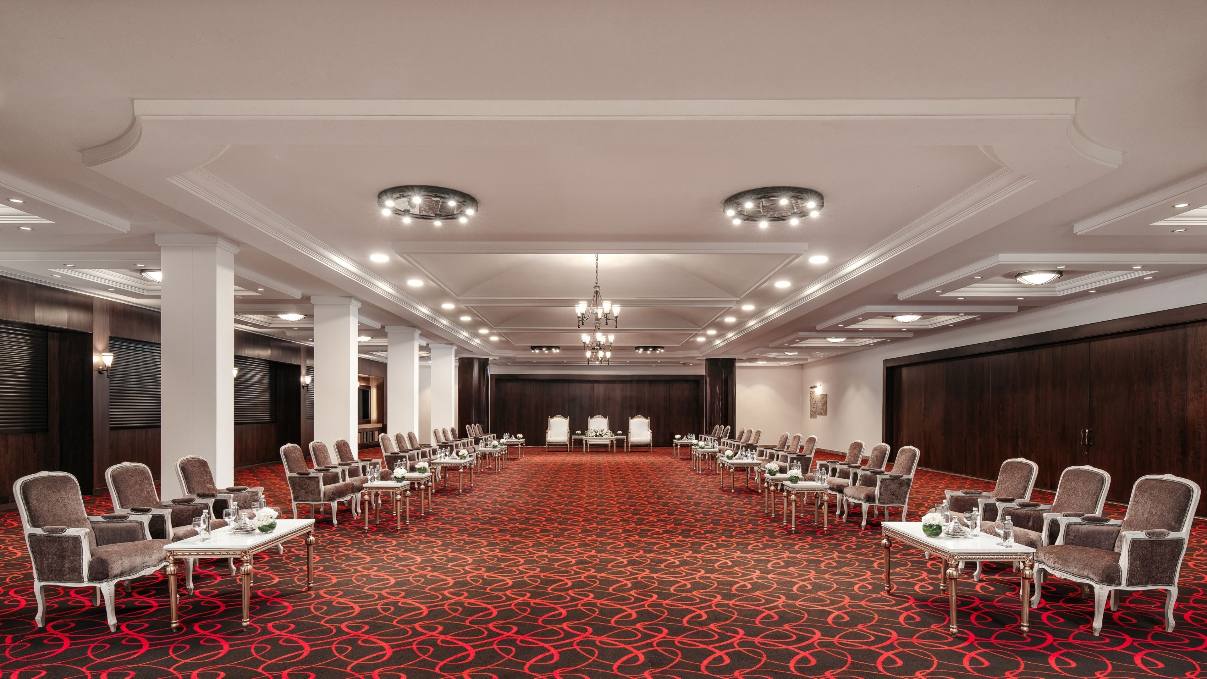Une salle de conférence avec un tapis rouge, des chaises blanches et un lustre.