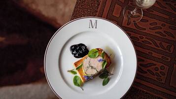 A plate with a dish, a glass of white wine, and a patterned tablecloth.