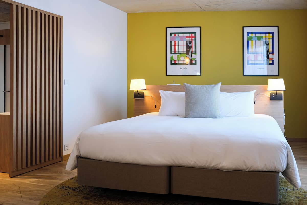 A hotel room with a bed, two wall-mounted lamps, and two framed pictures on the wall.