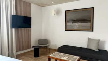 Een moderne hotelkamer met een houten vloer, een zwarte bank, een grijze fauteuil, een klein rond tafeltje en een groot abstract schilderij aan de muur.