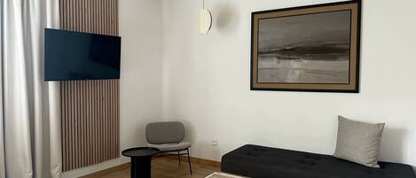 Una habitación de hotel moderna con piso de madera, un sofá negro, un sillón gris, una mesita redonda pequeña y un cuadro abstracto grande en la pared.