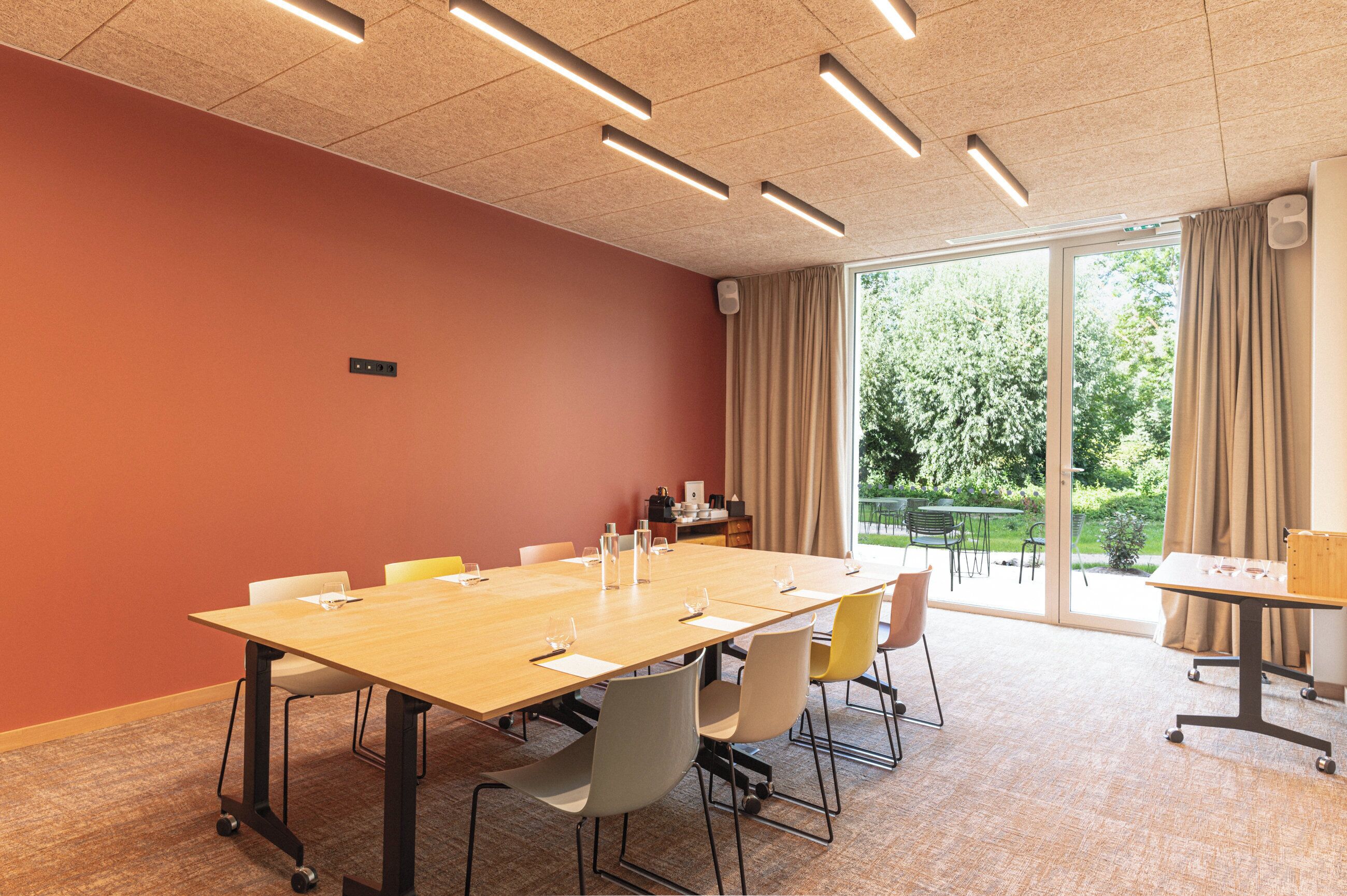 Un salón de conferencias con una mesa larga, sillas y un ventanal con cortinas.