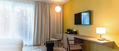 Habitación de hotel con una cama, un escritorio con lámpara, una silla, un televisor y una ventana con cortinas.