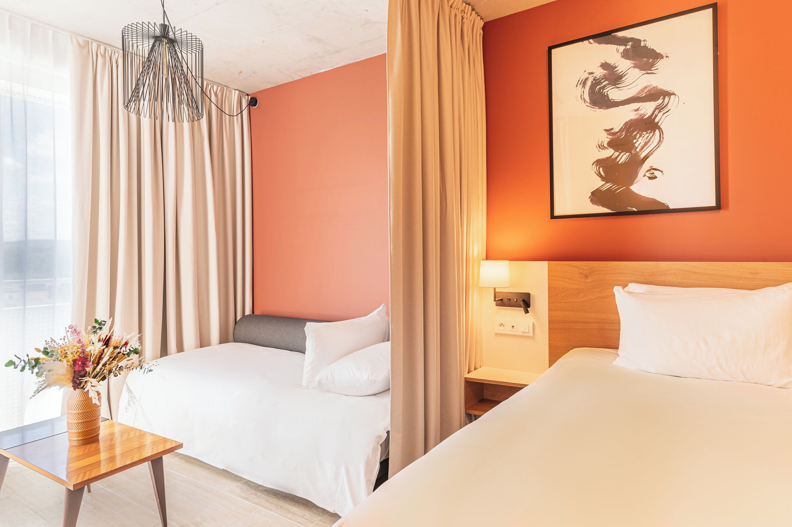 A hotel room with two beds, a wooden nightstand, a vase of flowers, and a painting on the wall.