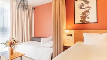 A hotel room with two beds, a wooden nightstand, a vase of flowers, and a painting on the wall.
